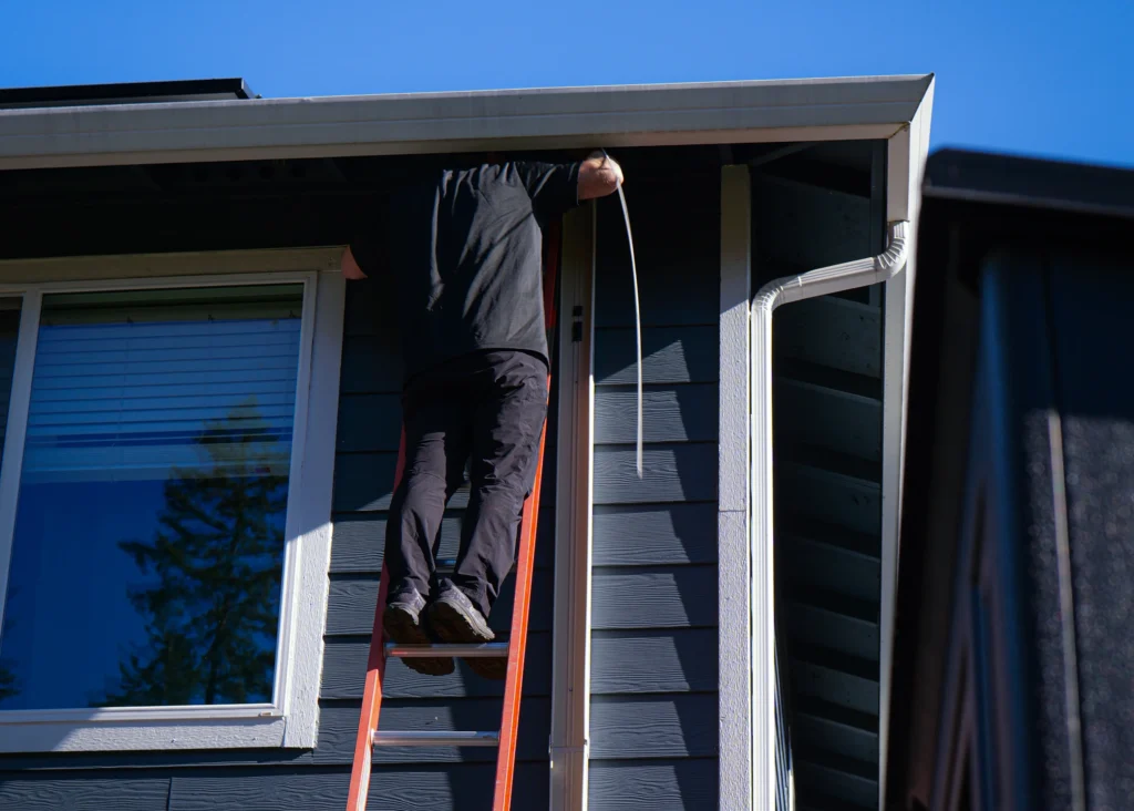 Technician working from a ladder at a home's roofline.