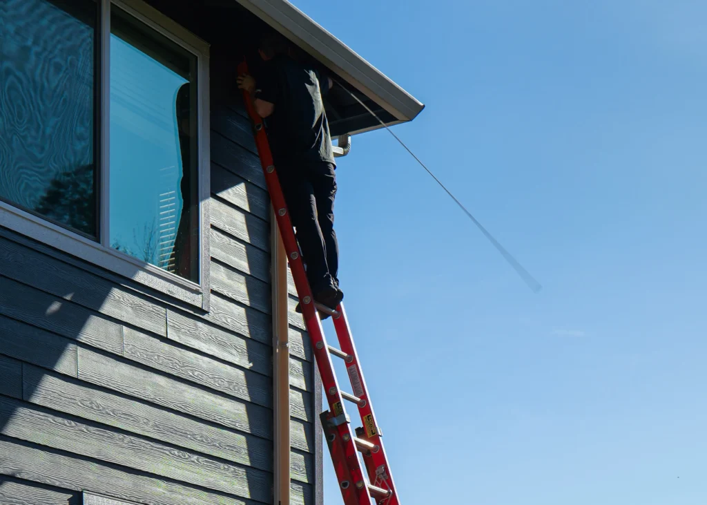 Technician working from a ladder beneath a home's roof eave.