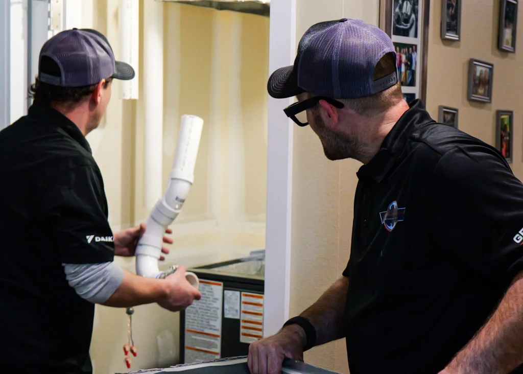 Two technicians fitting indoor HVAC equipment.